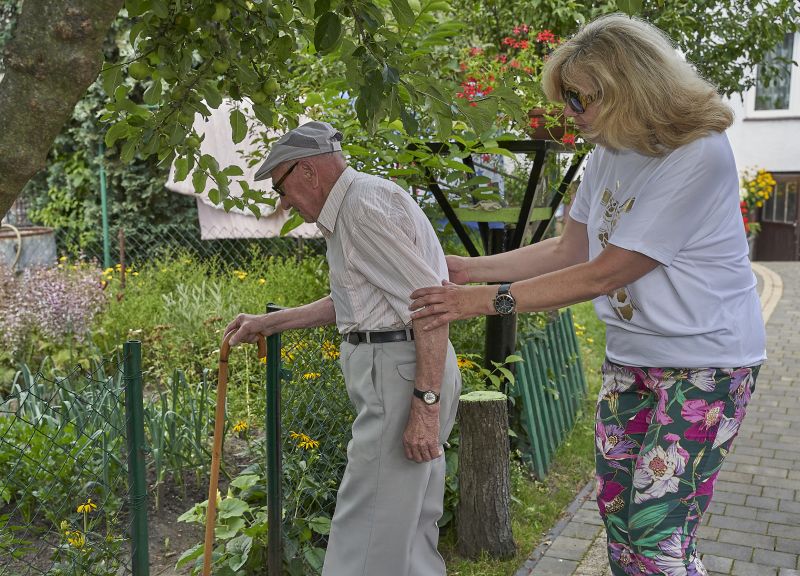 starszy pan w ogrodzie idzie o lasce korzystając z opieki kobiety